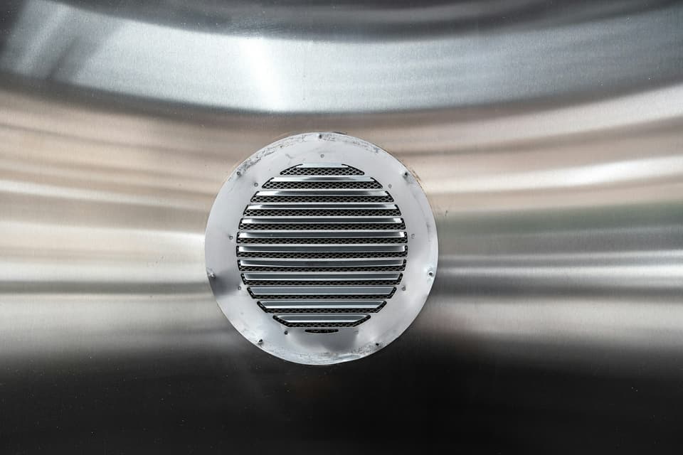 A round louvred metal air vent set into a brushed steel surface